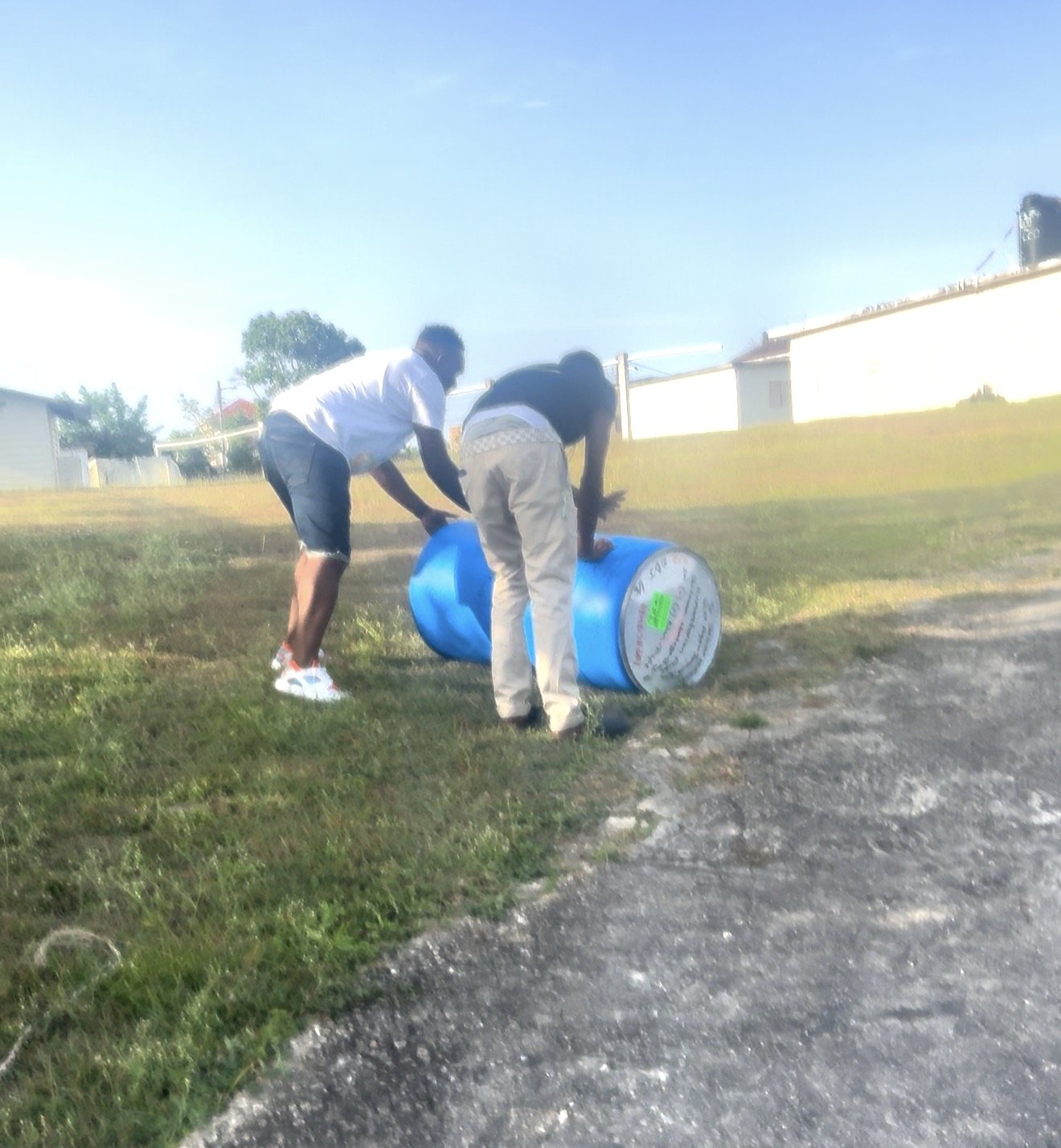 Two men rolling a Rise Again Jamaica Incorporated aid barrel across the churchyard in Trelawny.
