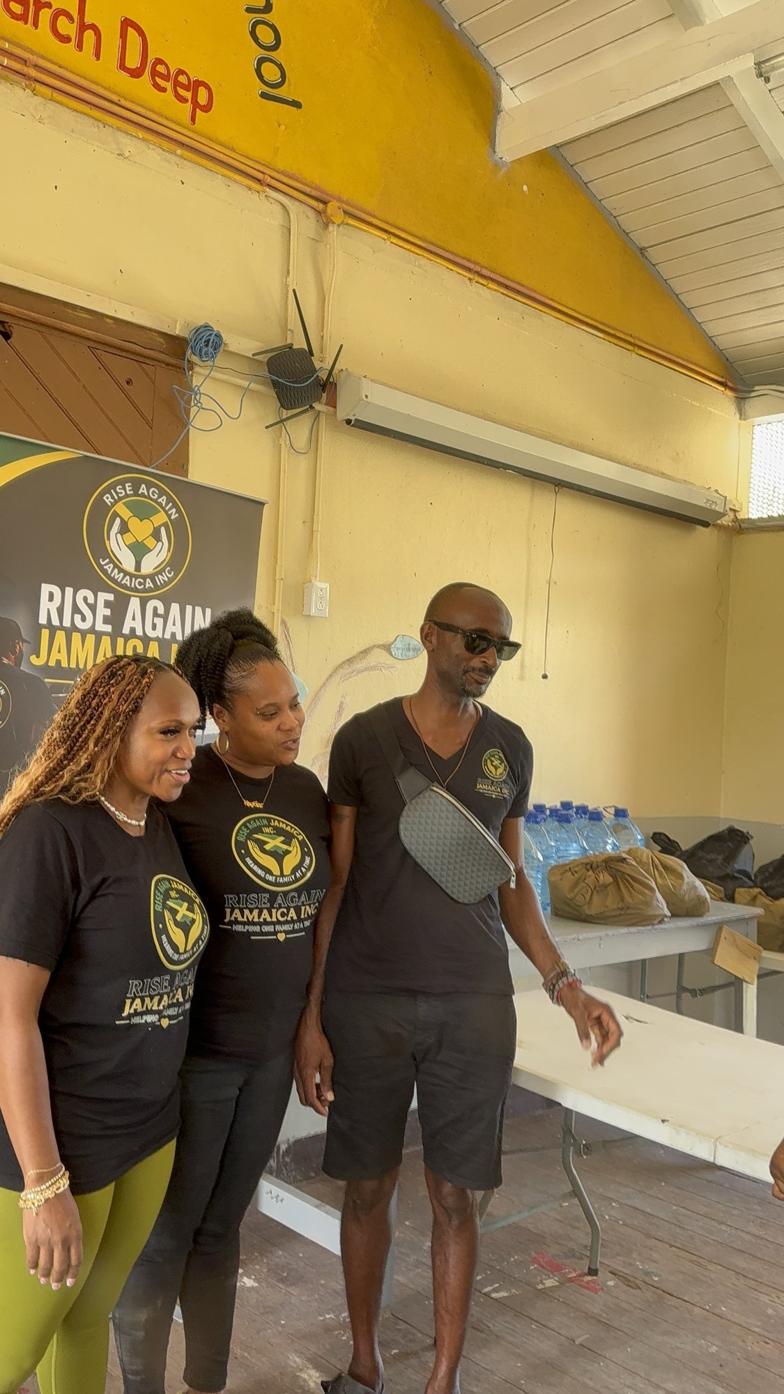 Three Rise Again Jamaica Incorporated team members in branded shirts at a school outreach.